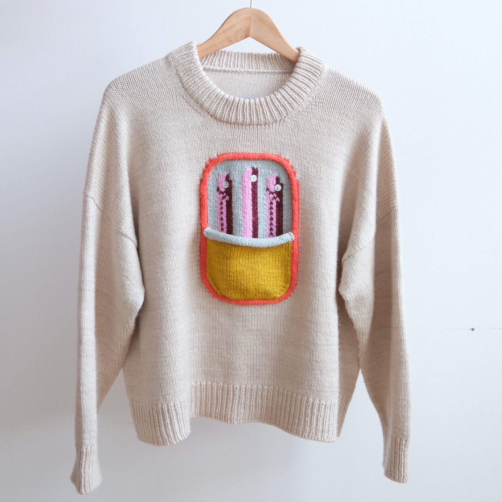 Beige sweater with a colorful embroidered pocket on a white background
