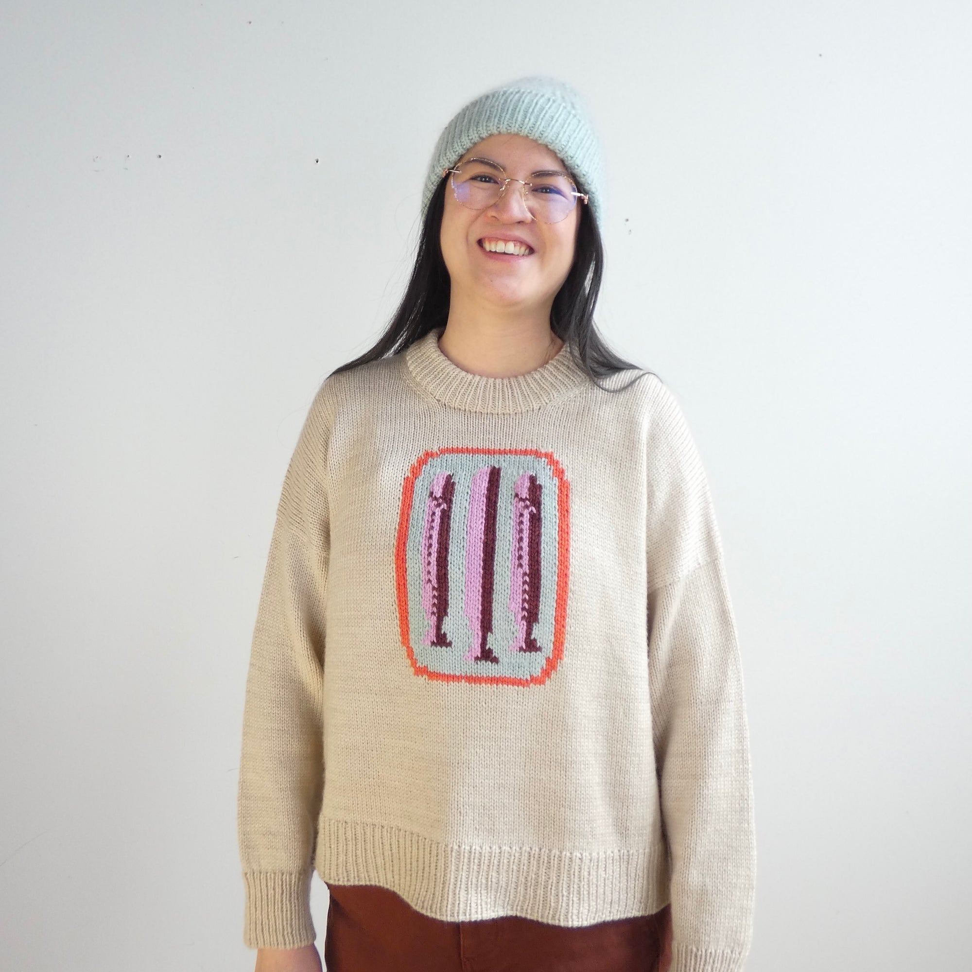 Person wearing a beige sweater with a colorful design on a plain background