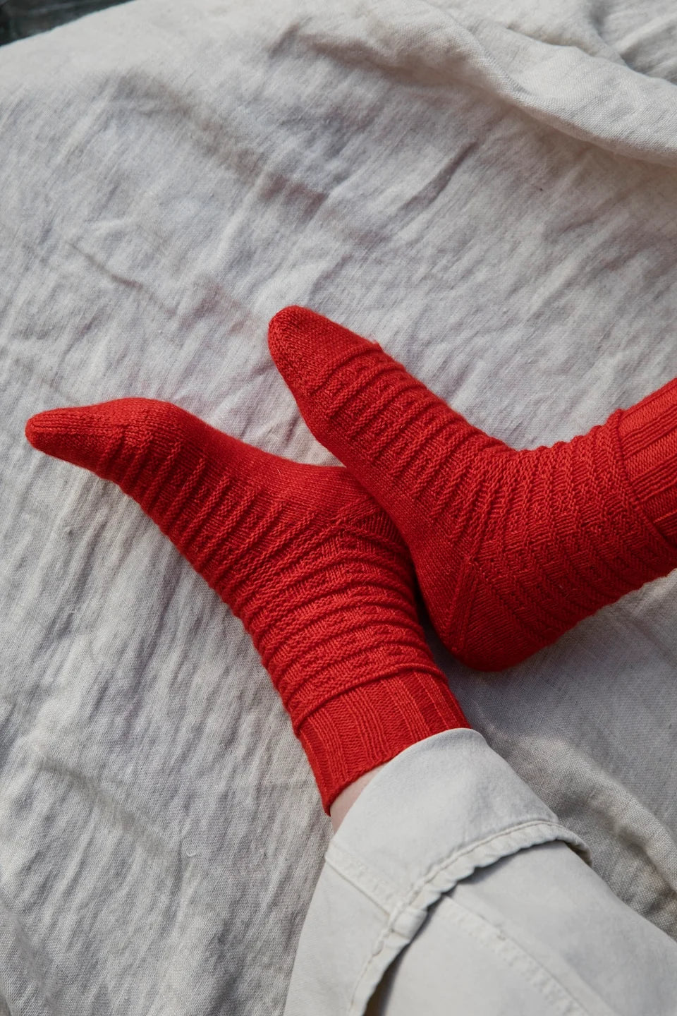A pair of feet wearing red, textured knit socks on a beige cloth.