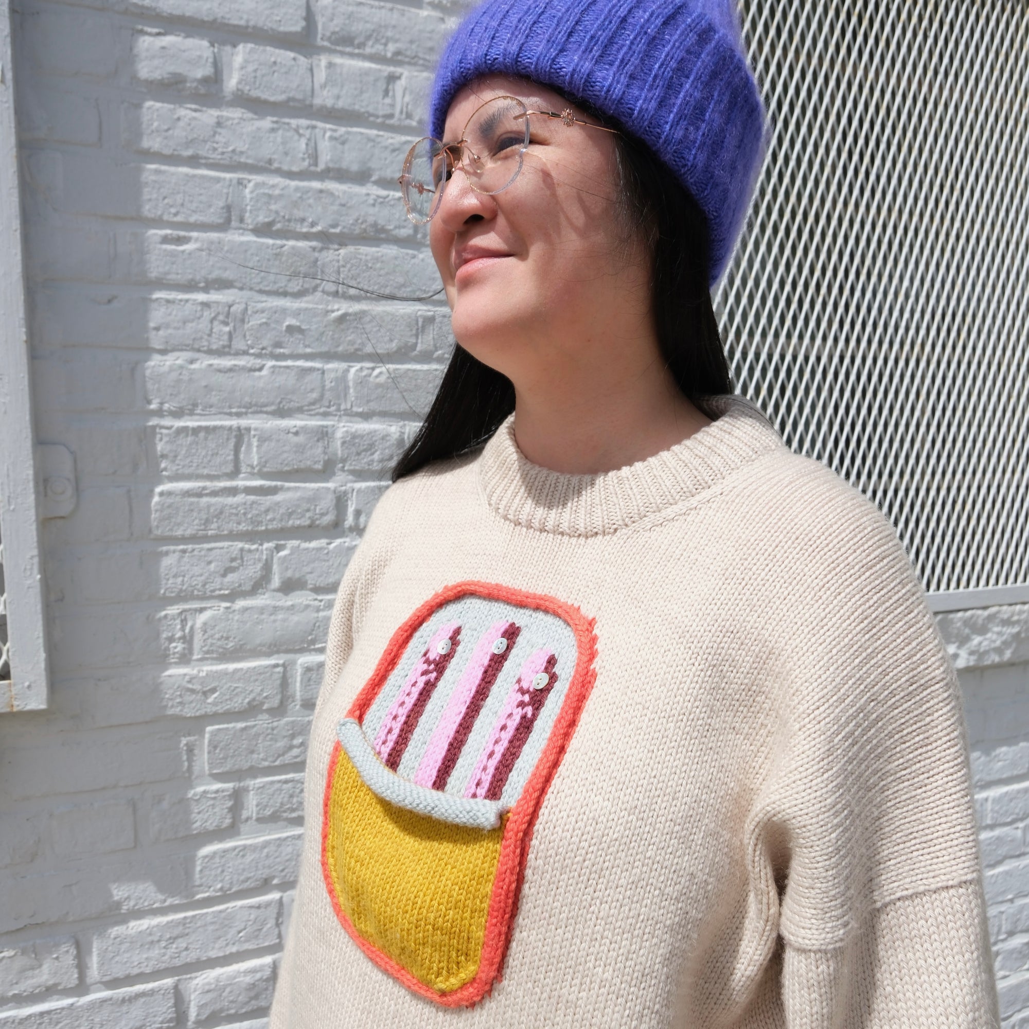 Person wearing a sweater with a colorful design against a gray brick wall.