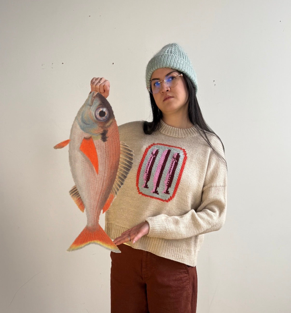 Person holding a fish-shaped object wearing a sweater with a colorful design.