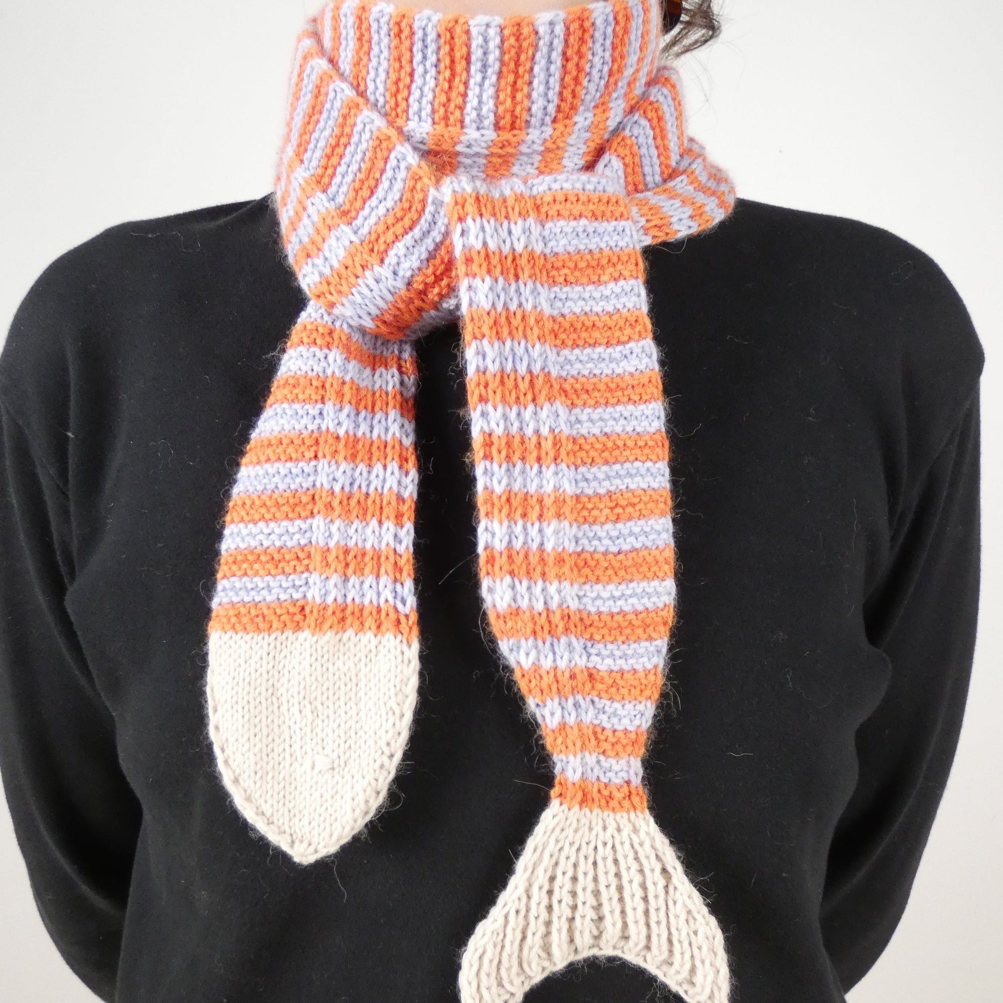 Person wearing a black shirt and a light blue and orange striped skinny scarf with a fish head and tail on the ends.