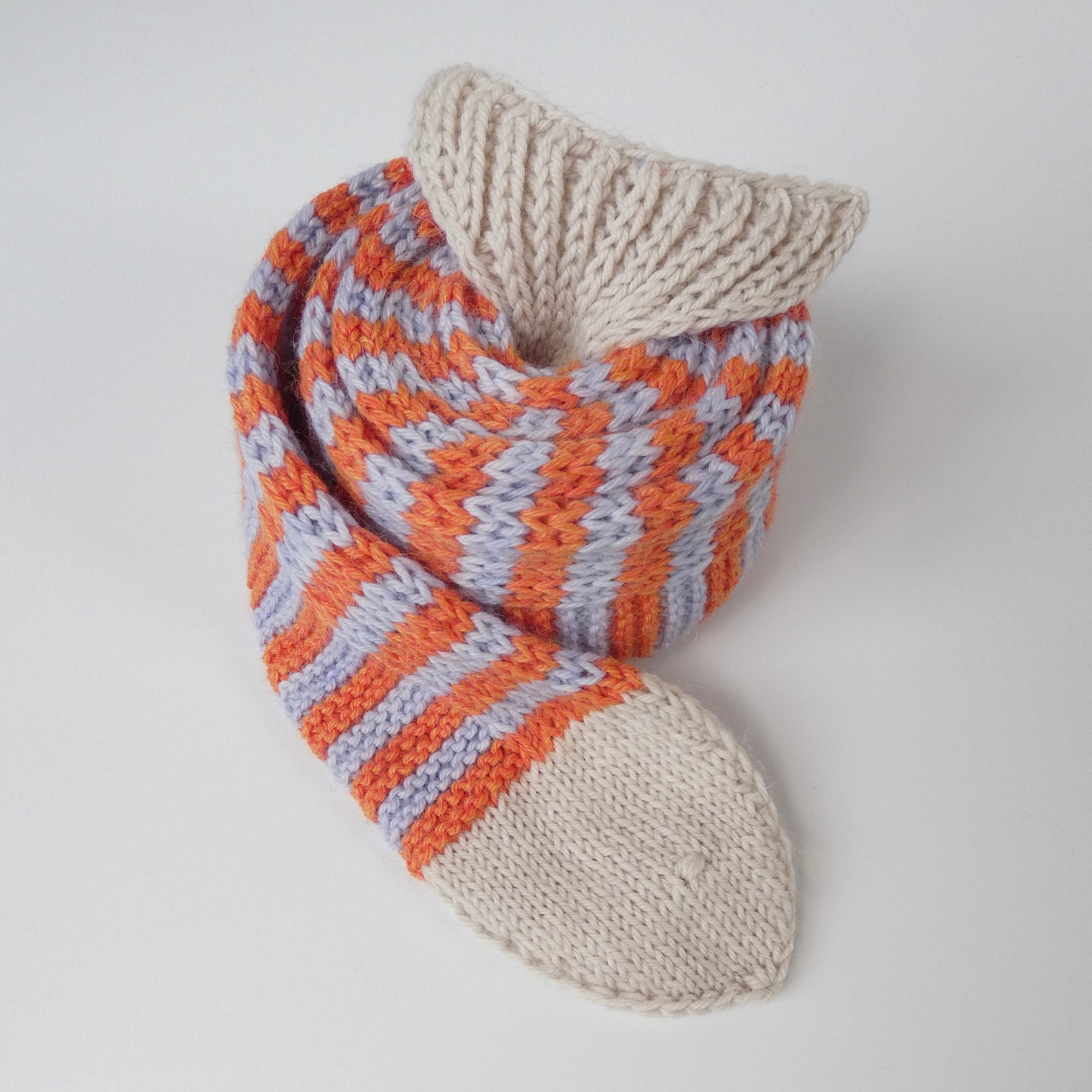 A rolled up knit skinny scarf in the shape of a fish with orange and light blue stripes on a white background.