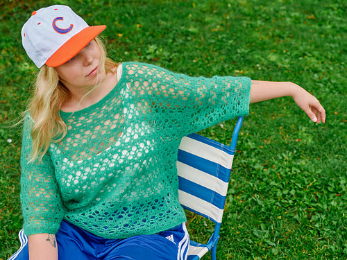 Person wearing a lacy green crochet sweater sitting on a lawn chair.