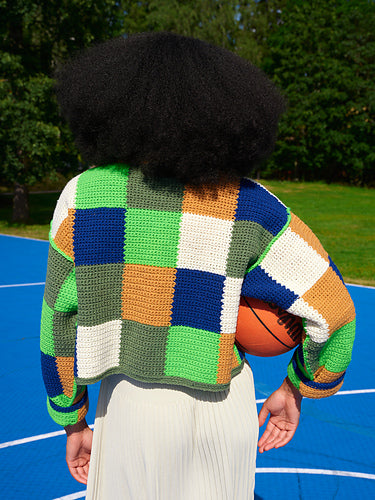 Person facing away wearing a colorful checkerboard crochet sweater and holding a basketball.