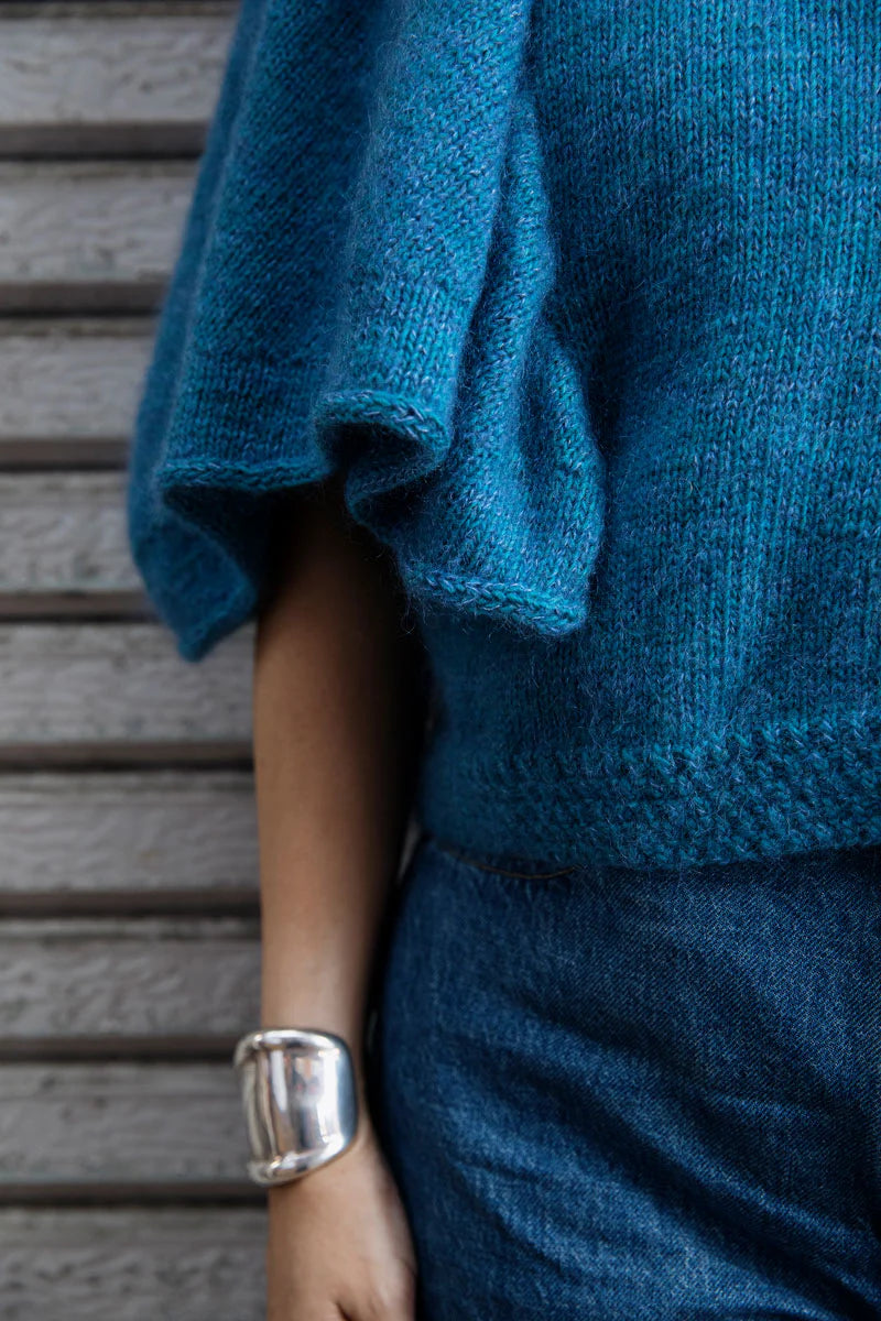 Close-up of a person wearing a teal knit sweater with wide 3/4 length sleeves.