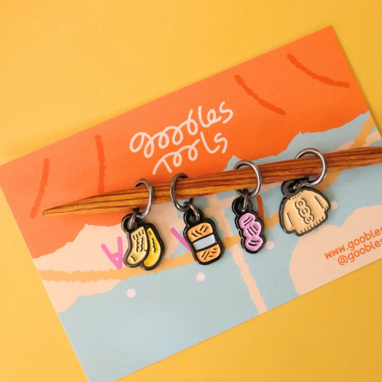 Set of colorful stitch markers on a knitting needle with a branded card in the background.