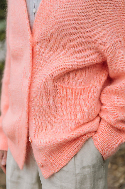 Close-up of a person wearing a pink knit cardigan with pockets.