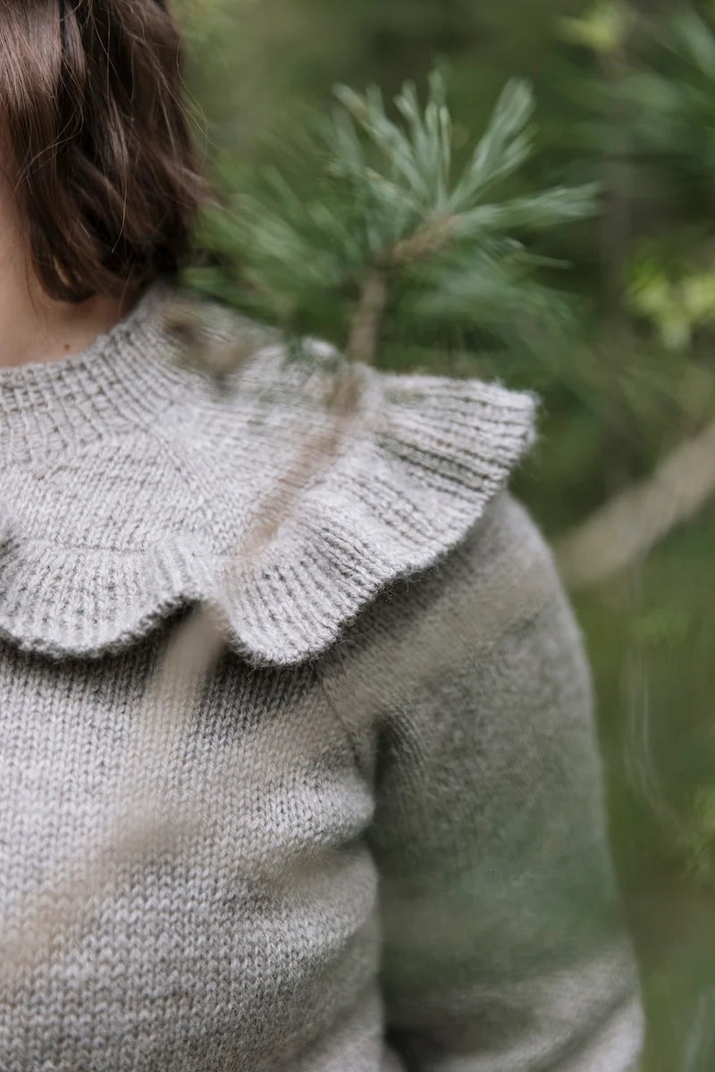 Close-up of a person wearing a gray knit sweater with a ruffled collar.