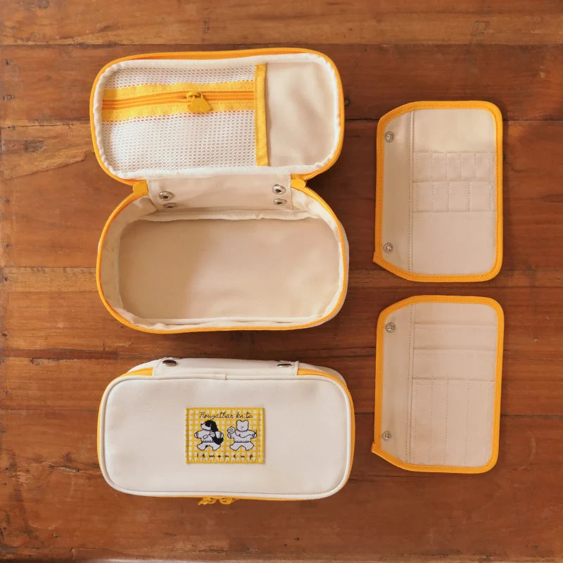 Two beige and yellow needle cases on a wooden surface. One is open, and the removable panels are located next to it.