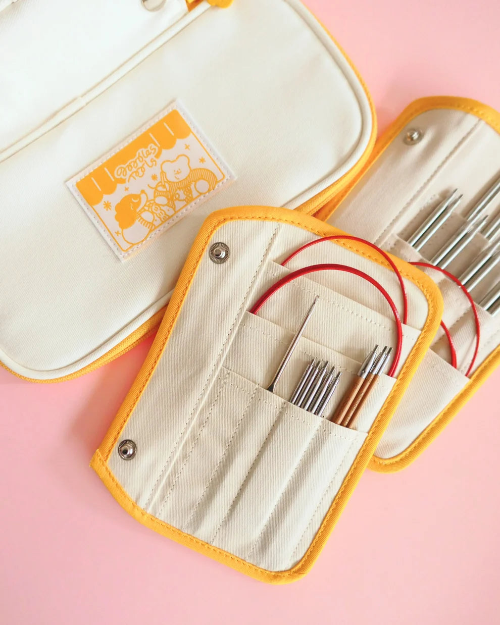 Set of knitting needles in a beige case with yellow trim on a pink background