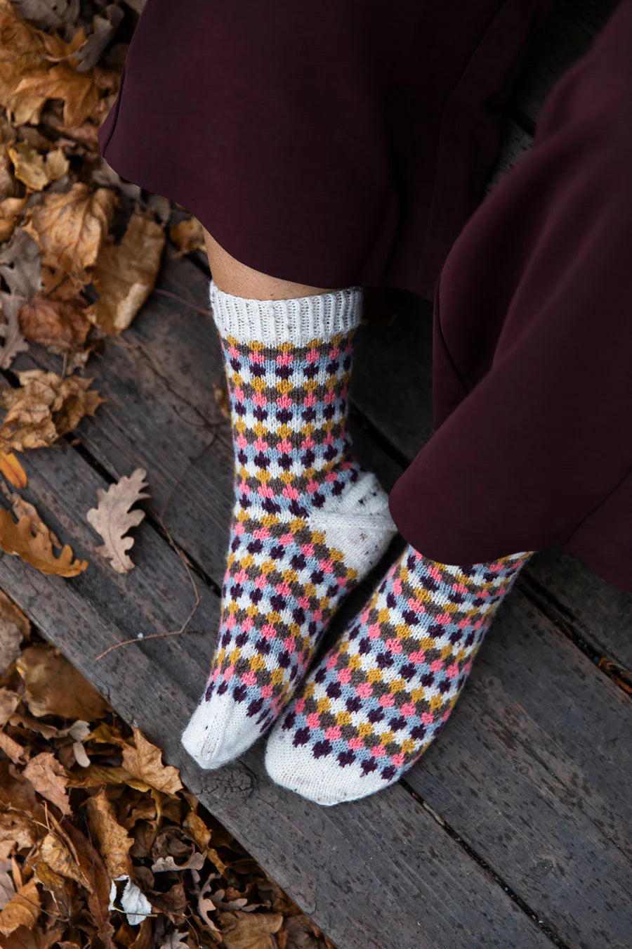 Person wearing patterned knit socks sitting on wooden steps with autumn leaves.