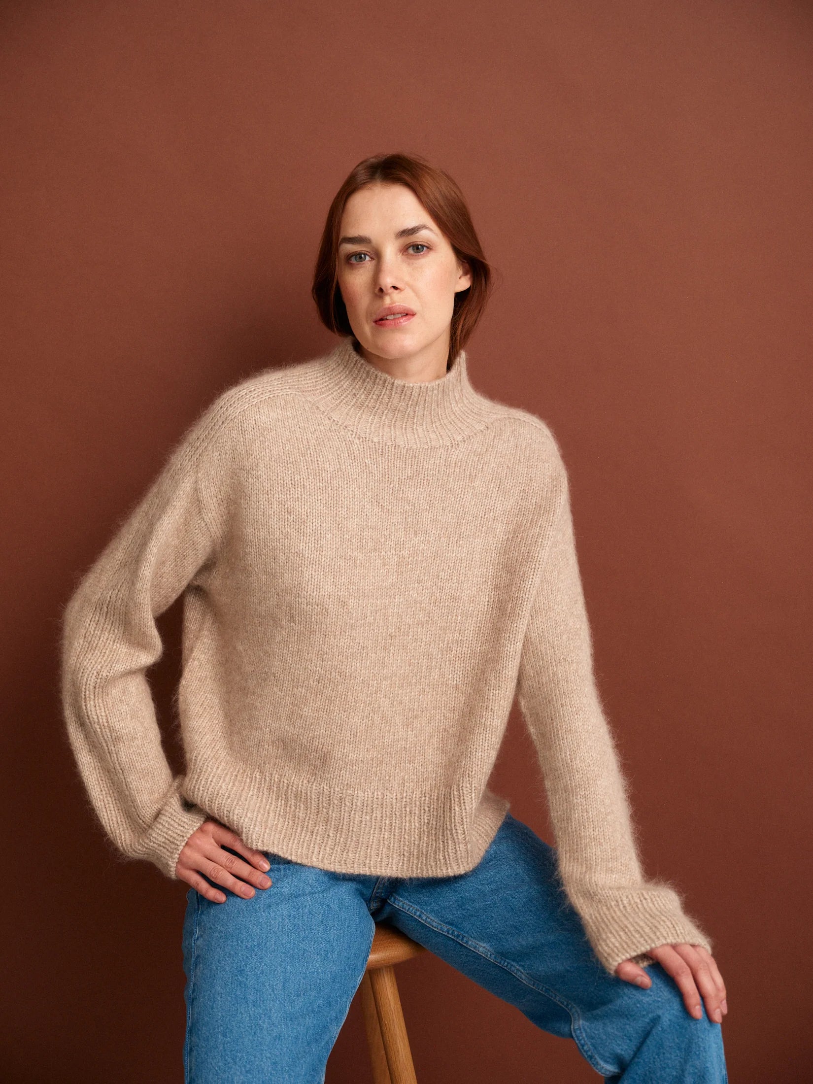 Person wearing a beige knit sweater against a brown background.