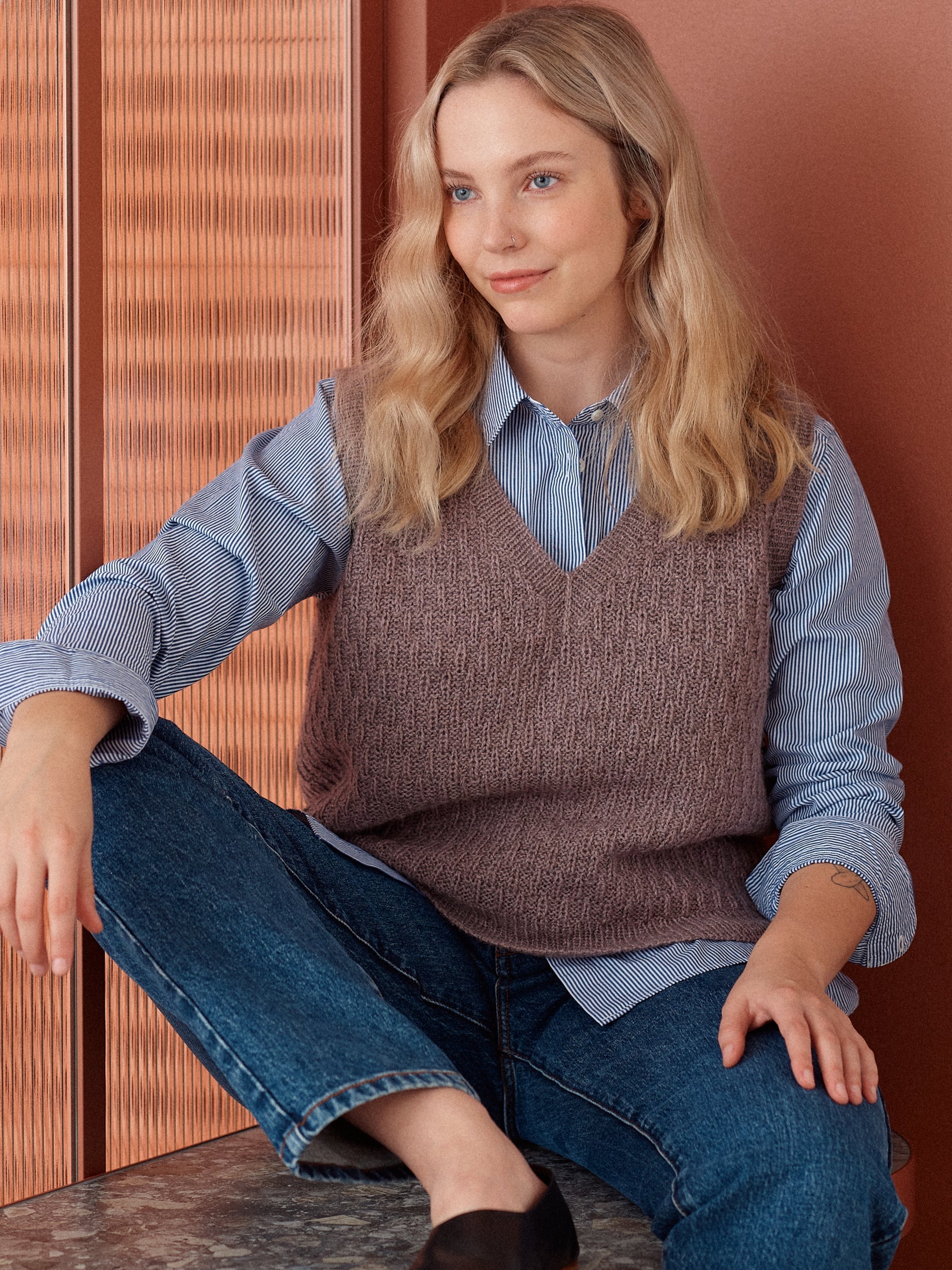 Person wearing a brown knit vest over a blue button-down shirt against a brown background.